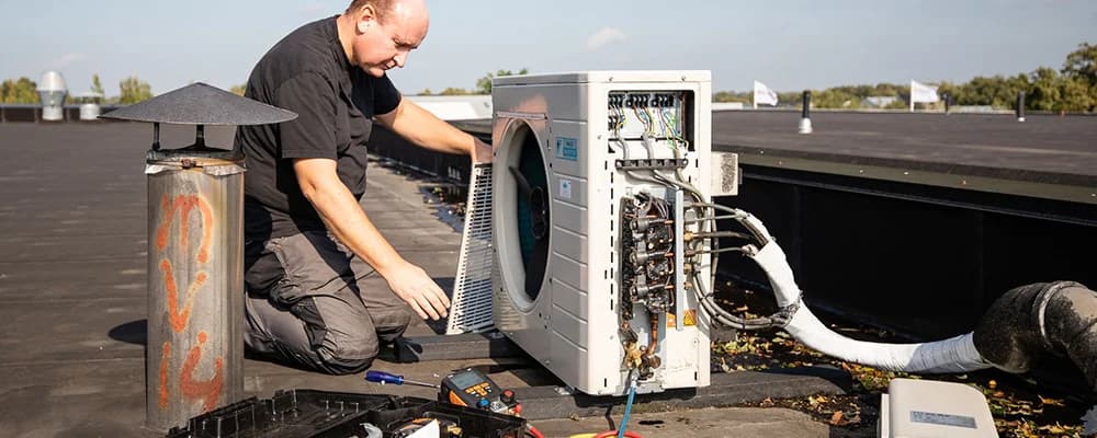 Monteur voert onderhoud uit aan een airco-buitenunit op een dak