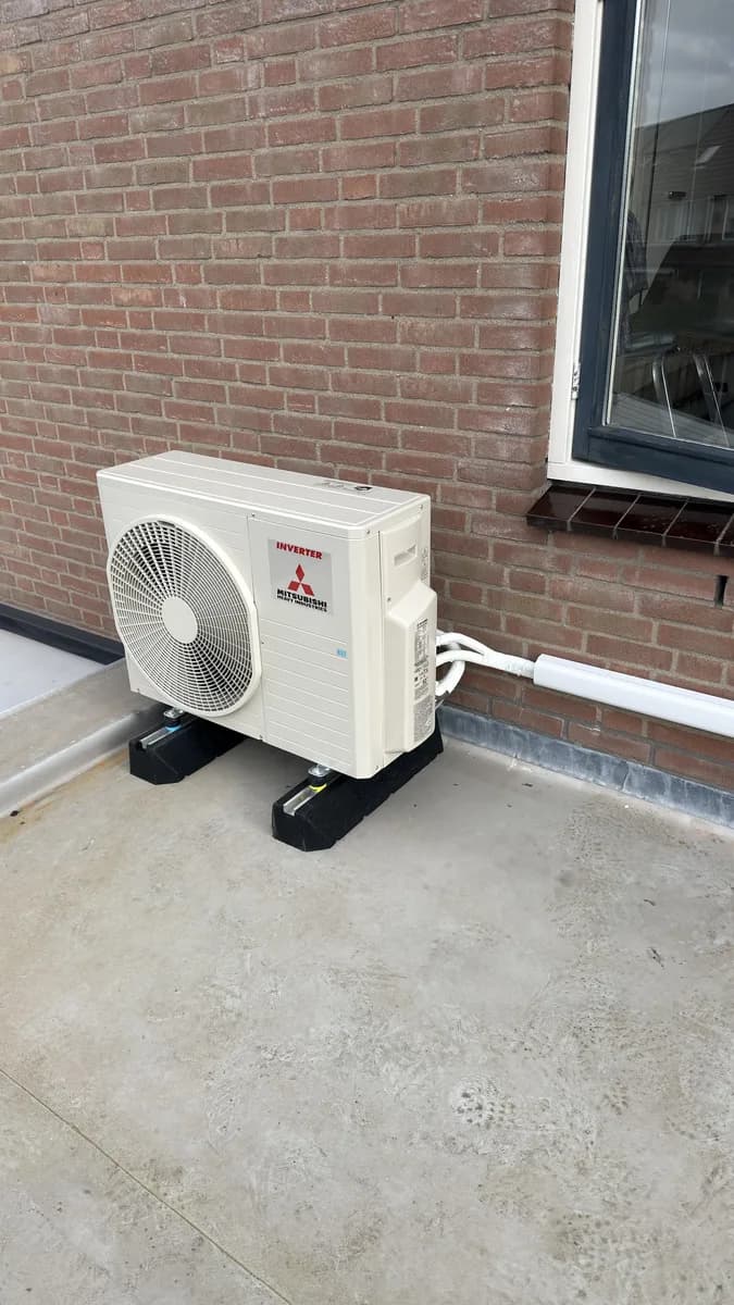Airco-buitenunit op een balkon tegen een bakstenen gevel