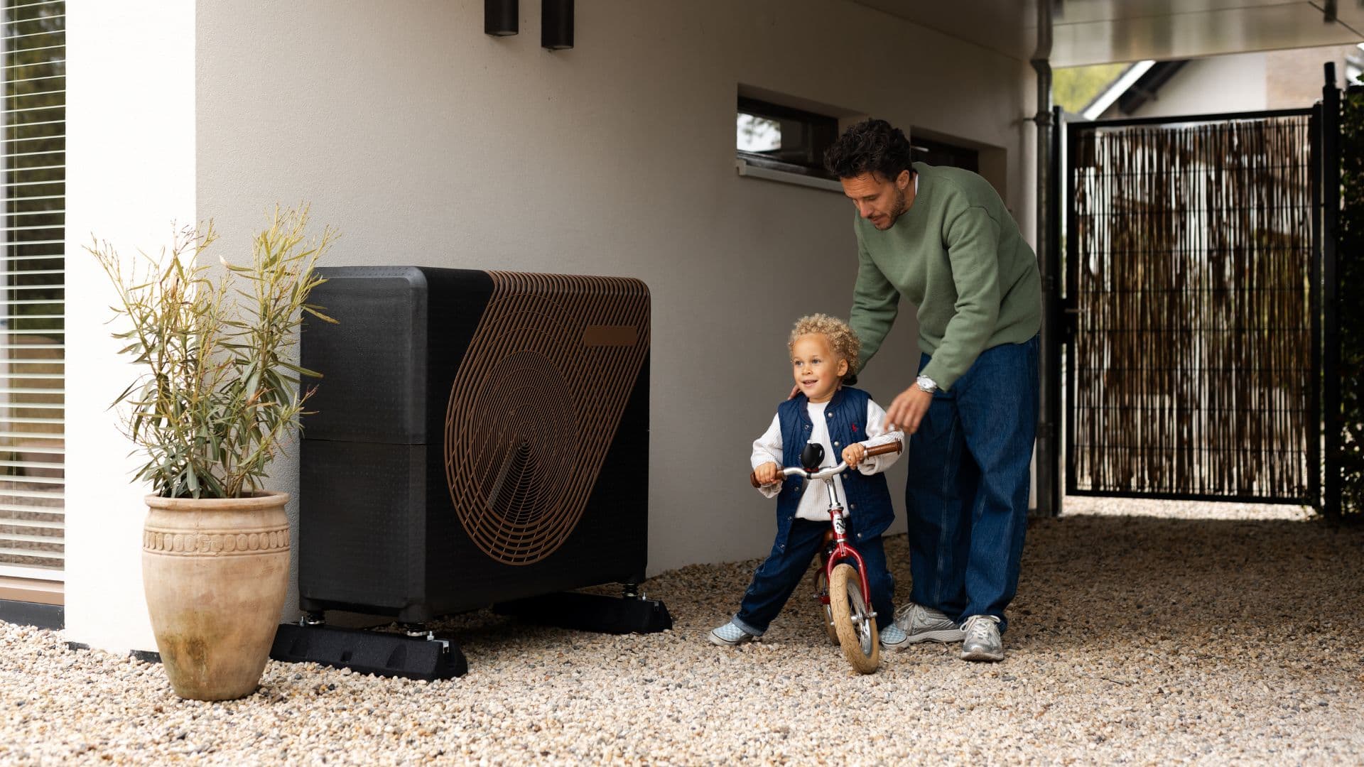 Warmtepomp-buitenunit naast een woning met een ouder en kind