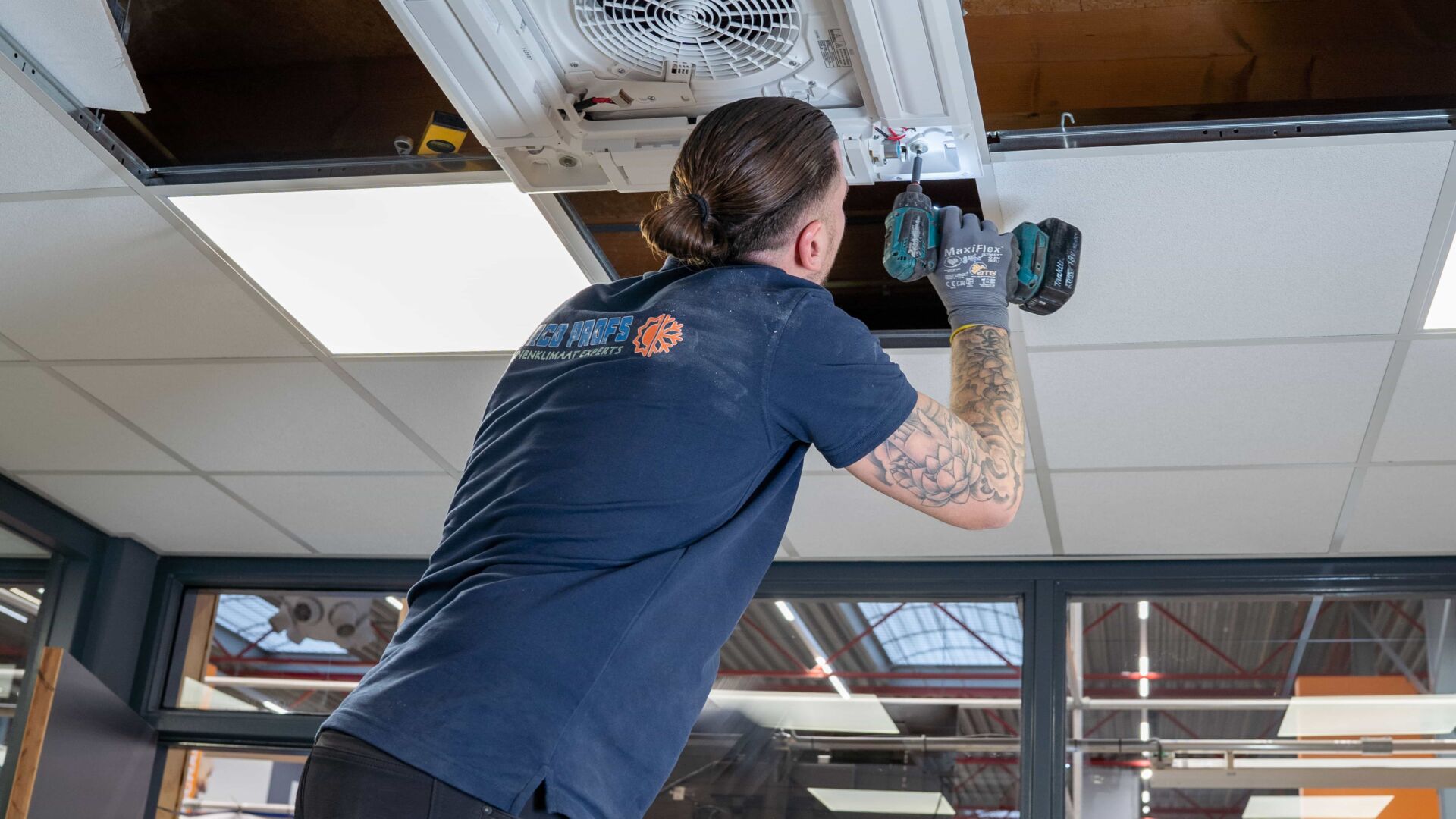 Monteur installeert airco-unit in systeemplafond met accuboormachine